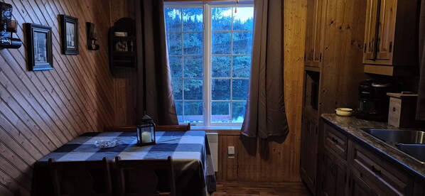 A wooden interior with a dining table, chairs, a window, and kitchen cabinets.