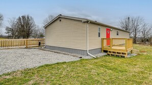 Ein einstöckiges Gebäude mit einer Holzterrasse und einer roten Tür, umgeben von Kies und Gras.