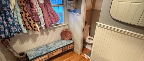 Una habitación pequeña y acogedora, con una banca, una ventana y una puerta que da a un baño.