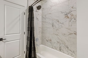 Un baño con una bañera blanca, azulejos de mármol y una cortina de ducha.