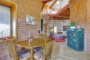 Un coin repas avec une table et des chaises en bois, un mur en briques, un escalier et un meuble contenant des objets décoratifs.