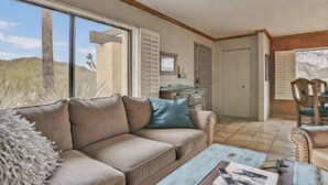 Ett vardagsrum med en beige soffa, ett soffbord och ett stort fönster med utsikt över kaktusar.