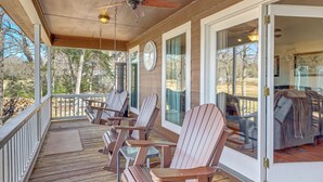Een overdekt terras met Adirondack-stoelen, een plafondventilator en uitzicht op de achtertuin.