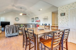 A spacious living room with a large TV, a sofa, and a dining area with wooden chairs and a table.