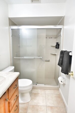 Een kleine badkamer met toilet, een douchecabine van glas, een handdoekrek en een wastafel met houten kastjes.