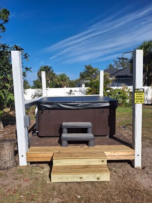 Een hottub met een houten terras en een trap, omgeven door een witte hek en palmbomen.