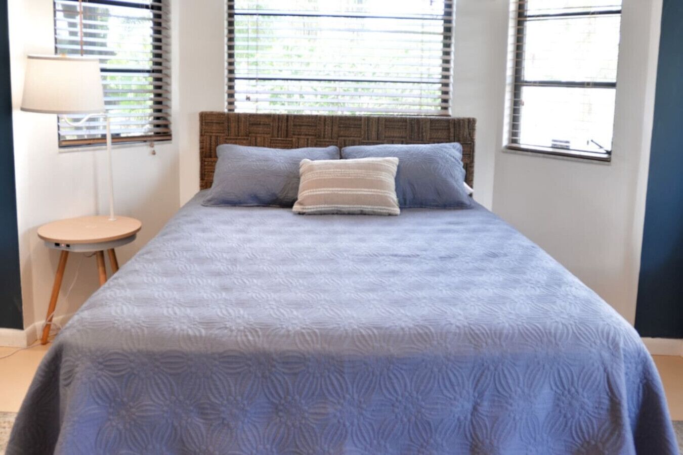 A bedroom with a bed, two windows, a lamp, and a small stool.