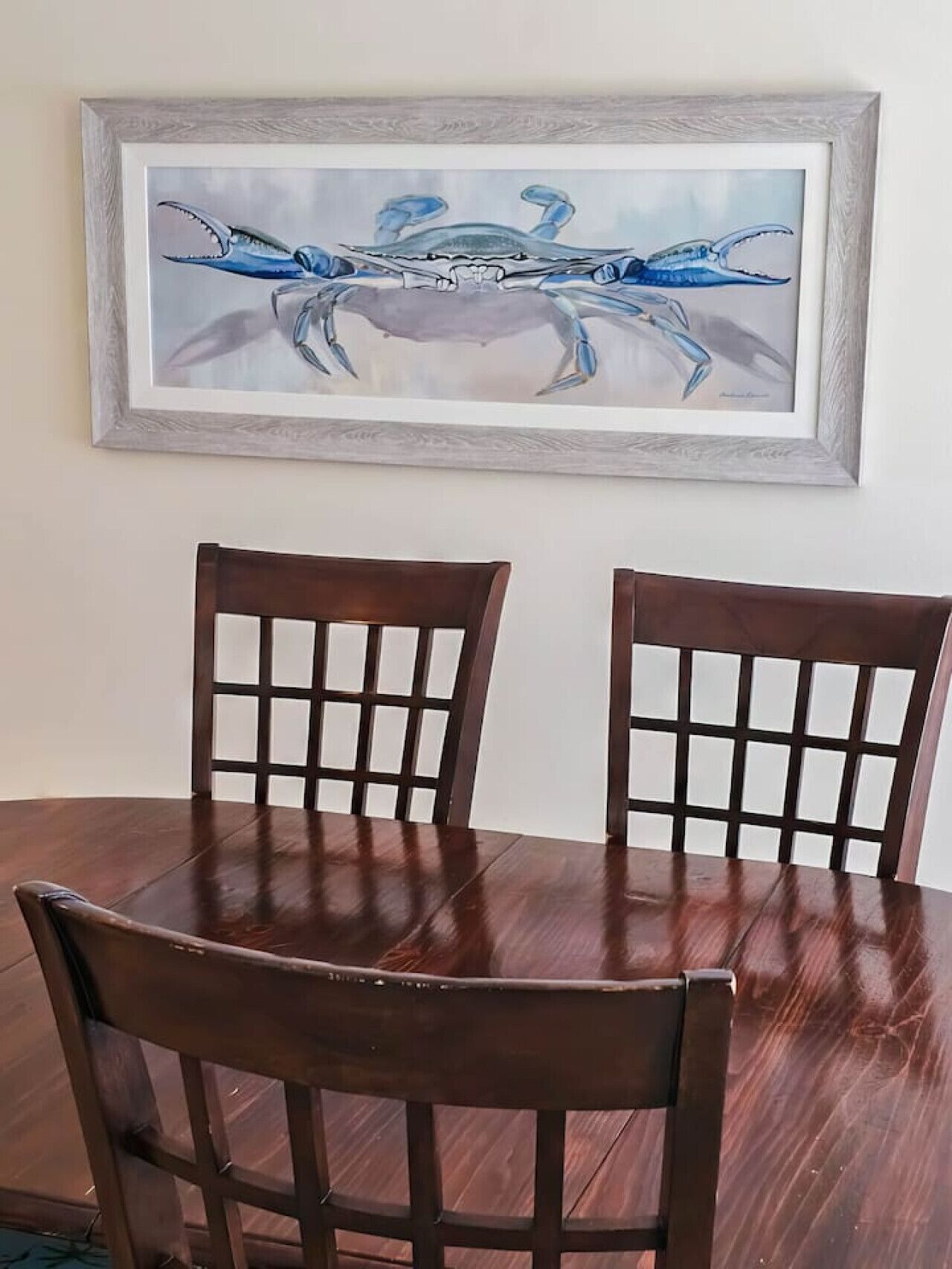 Uma mesa de jantar com duas cadeiras de madeira e um quadro na parede com a imagem de um caranguejo azul.