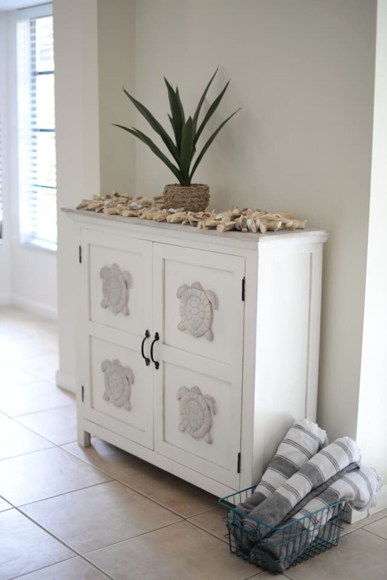 A white cabinet with decorative turtle motifs, a potted plant, and a basket with striped towels.