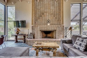 Un salón acogedor con chimenea de piedra, asientos cómodos y un amplio ventanal con vistas al exterior.