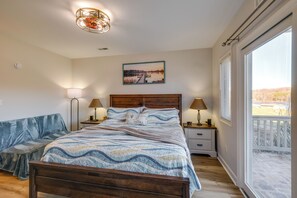 Un dormitorio con una cama de madera, una mesita de noche con una lámpara, un banco y un amplio ventanal con vistas al exterior.