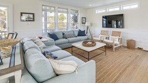 A spacious living room with a large sectional sofa, a coffee table, and two wicker chairs. - Family Friendly! Canal-Front Gem in Bethany Beach (Bethany Beach)