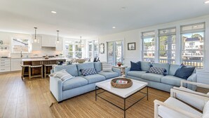 A spacious living area with a large sofa set, a coffee table, and a kitchen in the background. - Family Friendly! Canal-Front Gem in Bethany Beach (Bethany Beach)