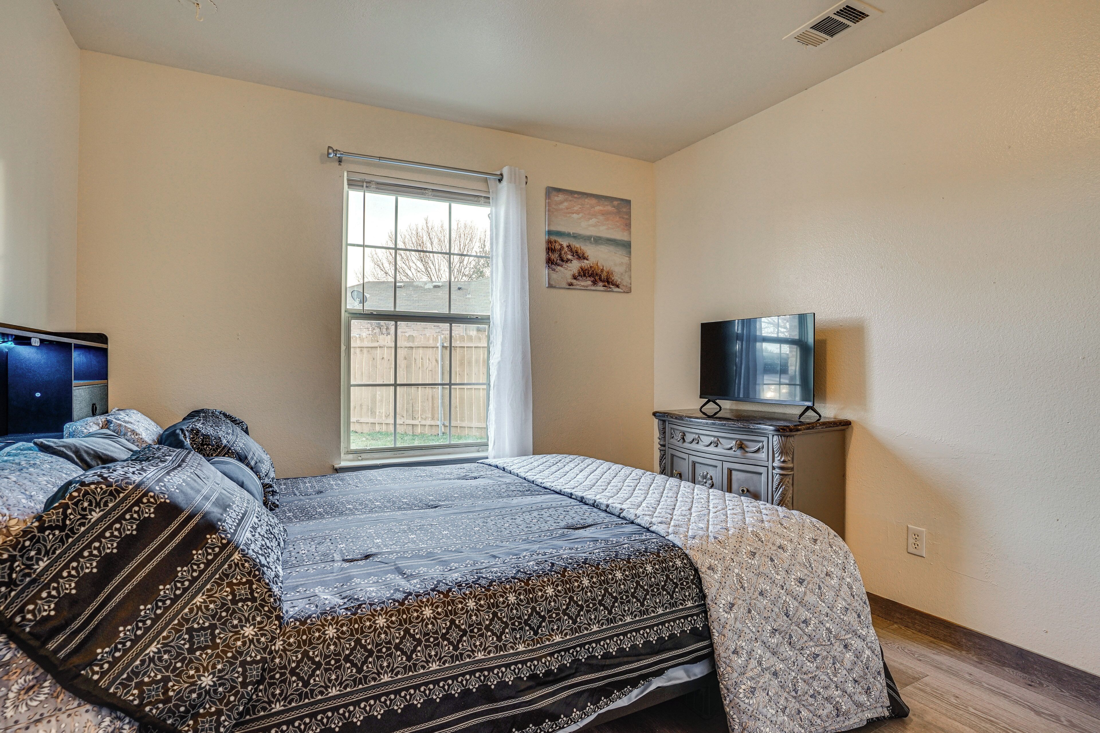 A bedroom with a large bed, a dresser, a television, and a window with a view of the outside.