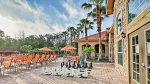 A chessboard set up on a paved patio with orange chairs and umbrellas, palm trees, and a building with a tiled roof. - Resort-Style Retreat w/ Private Patio in Davenport (Davenport)
