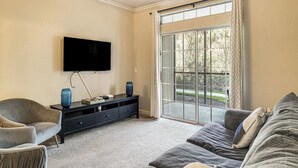 A living room with a flat-screen TV, a sofa, a chair, and a large window with curtains. - Resort-Style Retreat w/ Private Patio in Davenport (Davenport)