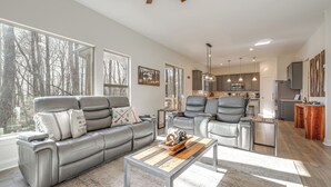 A modern living room with a grey leather sofa, a wooden coffee table, and a view of the kitchen in the background. - Lake Lure Getaway w/ Hot Tub & Fire Pit! (Lake Lure)