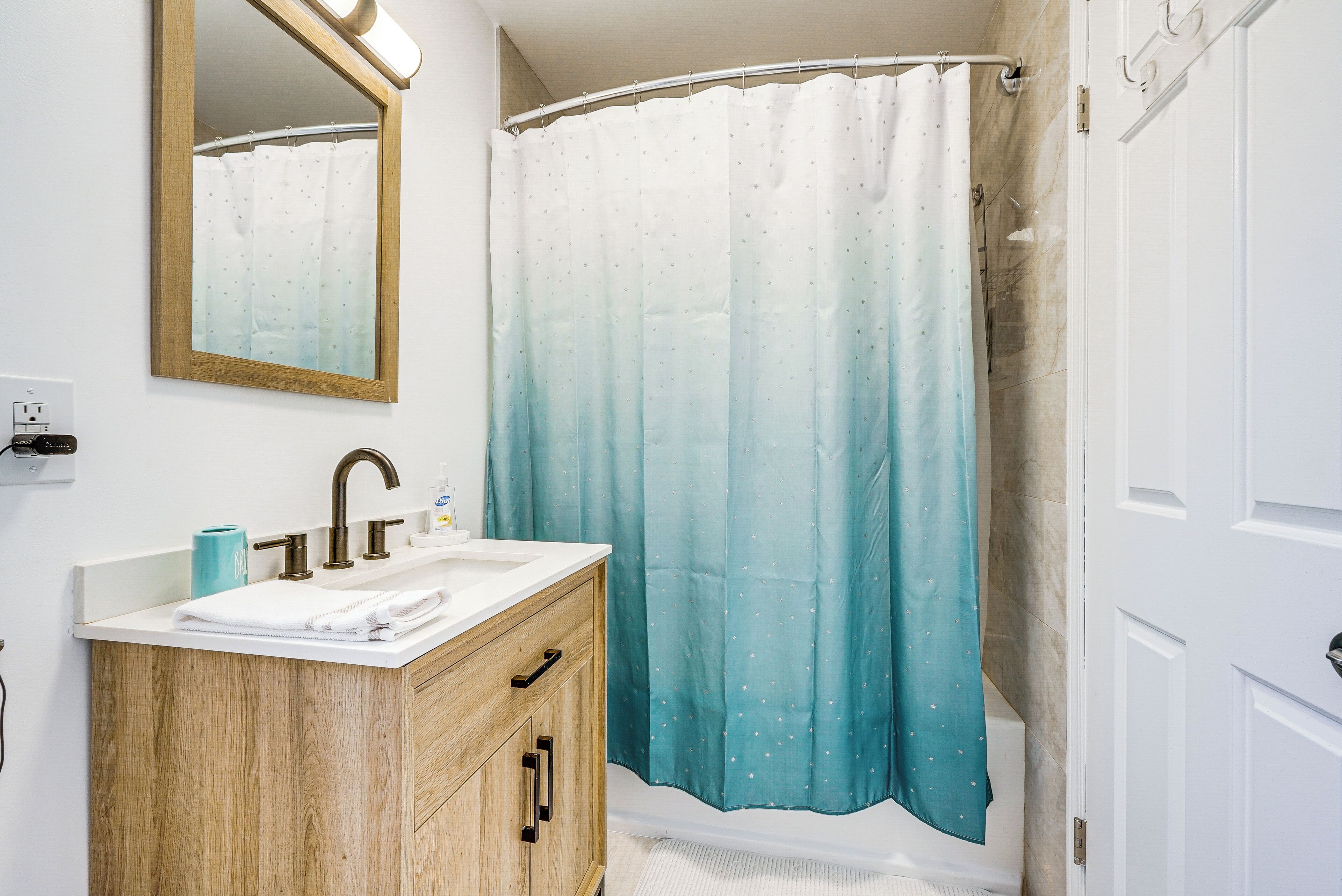 A bathroom with a wooden vanity, a mirror, a sink, and a shower curtain.