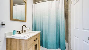 A bathroom with a wooden vanity, a mirror, a sink, and a shower curtain.