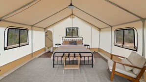 A tented room with a bed, a chair, and a small table.