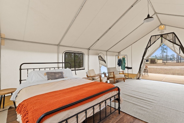 A tented accommodation with a bed, chairs, and a view of the outside.