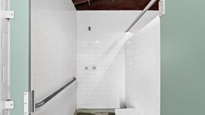 Un pequeño box de ducha con azulejos, una barra de apoyo metálica y un cabezal de ducha.