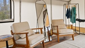 Una habitación tipo tienda de campaña con dos sillones color beige, una mesita y un perchero con varias prendas de vestir.