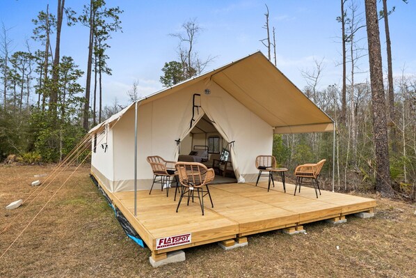 Une cellule d’habitation pour camping-car montée sur un châssis plat, dotée d’un porche couvert, de quatre chaises en osier et d’une table à manger.