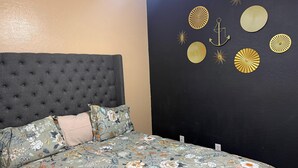 Un dormitorio con cabecera capitonada, colcha de flores y decoración mural.