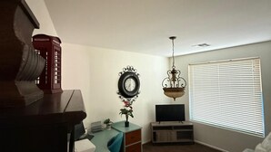 Una sala de estar con escritorio, televisión, candelabro y ventana con persianas.
