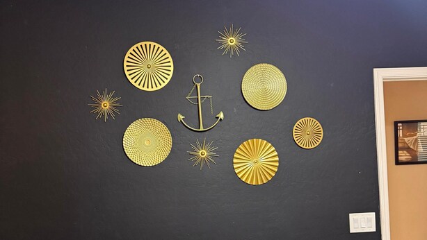 Una pared negra con detalles decorativos dorados, incluyendo un ancla y motivos que recuerdan al sol.
