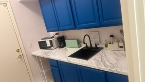 Una cocina con armarios azules, una encimera blanca, un microondas, un tostador, una cafetera y un fregadero.