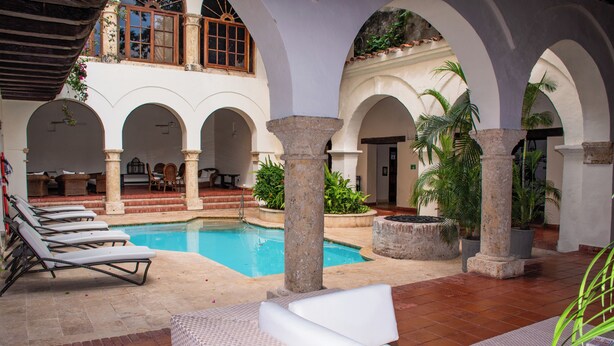 A pool area with lounge chairs and a dining table. - Charming Colonial Studio with Balcony on Santo Domingo Square + Pool (Cartagena de Indias)
