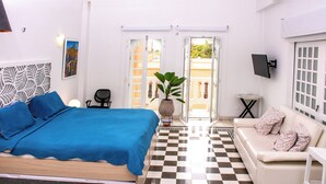 A hotel room with a bed, a sofa, a small table, a chair, and a potted plant. - Charming Colonial Studio with Balcony on Santo Domingo Square + Pool (Cartagena de Indias)