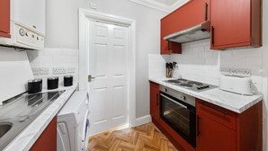 Una cocina con una puerta blanca, armarios rojos, una estufa, horno y lavadora.