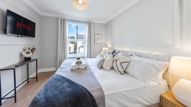 Una habitación de hotel moderna con una cama grande, un televisor de pantalla plana en la pared, una mesita de noche y vistas al exterior a través de una ventana.