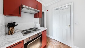 Una cocina con armarios rojos, salpicadero blanco de azulejos, estufa y puerta blanca.