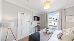 Un dormitorio con cama, televisión, lámpara, ventana con vistas y una puerta.