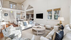 A spacious living room with a high ceiling, a staircase leading to an upper level, and a modern kitchen in the background. - Private Beach Access | Bikes | Patio (Watersound)