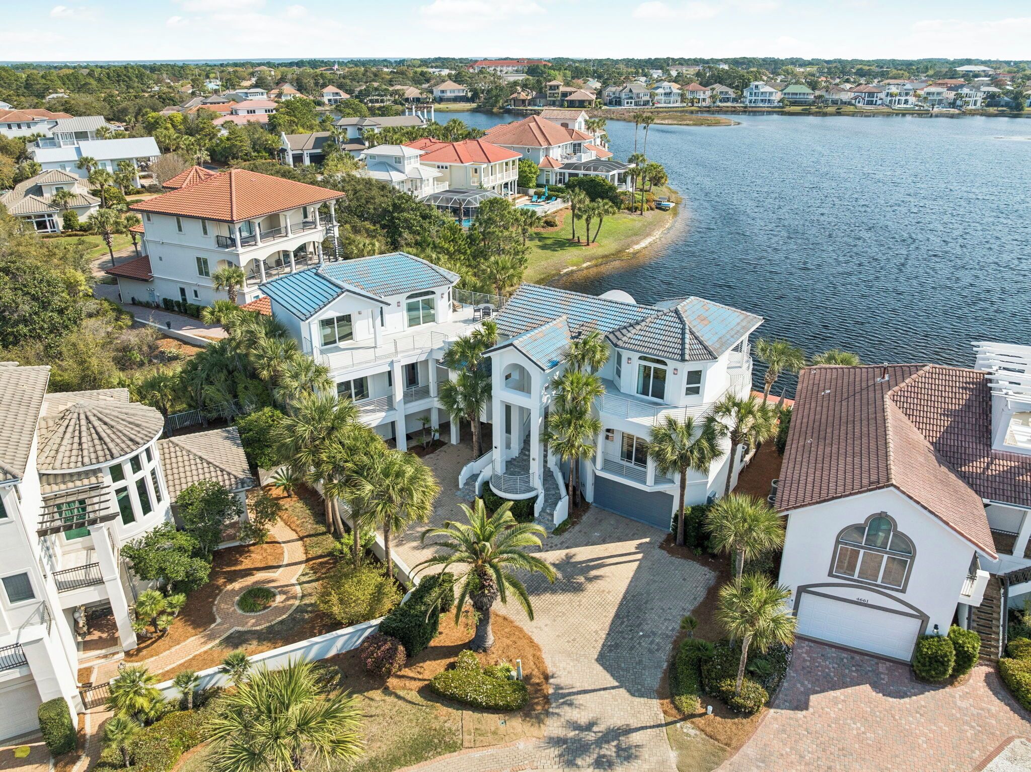 A residential area with houses near a lake, featuring a central house with a large driveway and a pool.