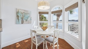 Un espace repas avec une table blanche, des chaises, un luminaire suspendu et une vue sur l’extérieur.