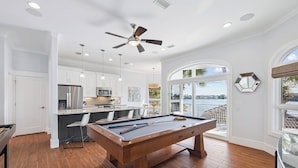 Une table de billard dans une pièce dotée d’un plancher en bois, de murs blancs et d’un ventilateur de plafond.