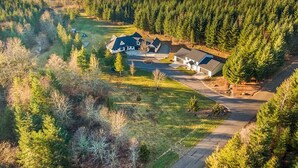 En stor bolig omgivet af tæt skov, med velholdt græsplæne og en indkørsel til indgangen.