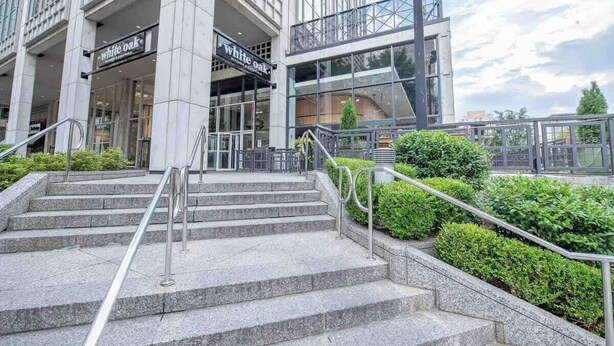 A modern building with a glass facade, a staircase leading to an entrance, and a sign for 'White Oak'. - 1BR Condo w/City Views by Peachtree (Atlanta)