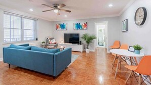 A modern living room with a blue sofa, a TV, and a dining area with orange chairs. - 1BR Condo w/City Views by Peachtree (Atlanta)