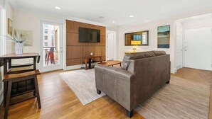 A modern living room with a sofa, a TV mounted on the wall, and a dining area with a table and chairs. - Downtown Atlanta Condo  Walk to Everything (Atlanta)