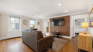 A spacious living room with a large sofa, a flat-screen TV mounted on a wooden panel, and a small table with a lamp. - Downtown Atlanta Condo  Walk to Everything (Atlanta)
