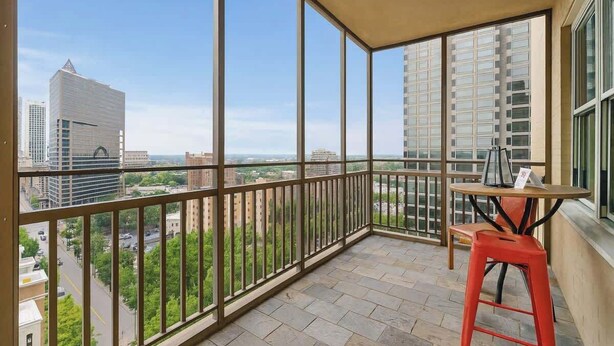 A balcony with a table and chair, offering a view of city buildings and greenery. - Downtown Atlanta Condo  Walk to Everything (Atlanta)