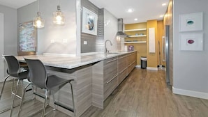 Een moderne keuken met een centraal eiland, barstoelen, hanglampen en uitzicht op de aangrenzende eetruimte.