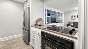 Ett modernt kök med vita skåp, ett kylskåp i rostfritt stål, en svart diskmaskin och en bänkskiva i trä.